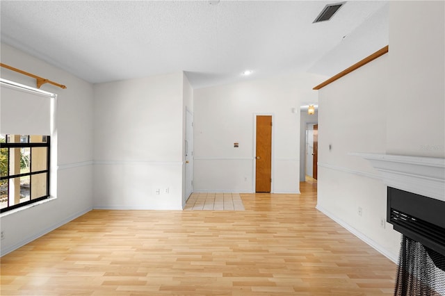 unfurnished living room with lofted ceiling, a textured ceiling, and light hardwood / wood-style flooring