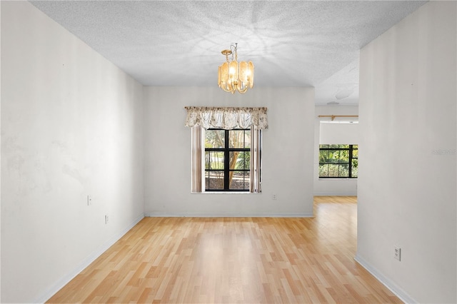 empty room with a notable chandelier, a textured ceiling, and light wood-type flooring