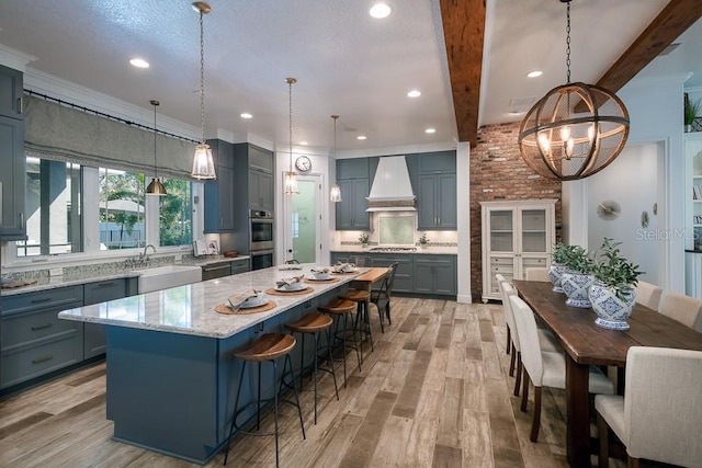 kitchen featuring premium range hood, a kitchen island, beamed ceiling, sink, and light hardwood / wood-style floors