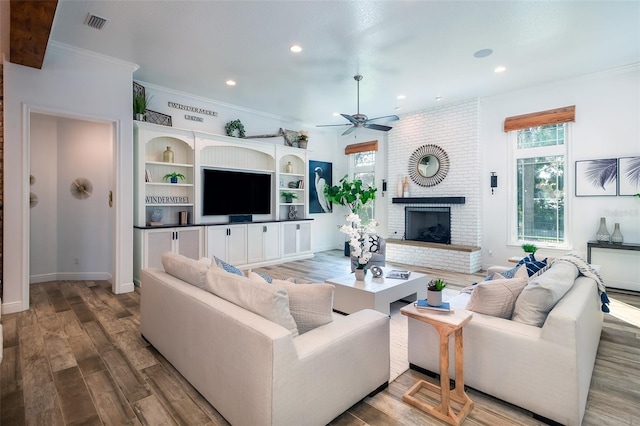 living room with a brick fireplace, crown molding, ceiling fan, and light wood-type flooring