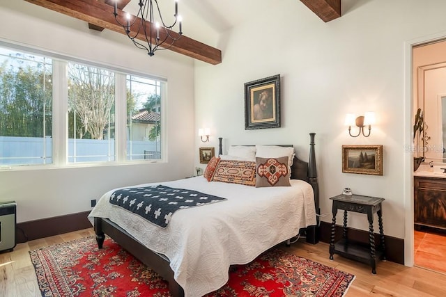 bedroom featuring beamed ceiling, ensuite bathroom, an inviting chandelier, and light hardwood / wood-style floors