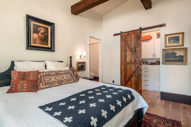 bedroom featuring beamed ceiling, ensuite bathroom, a barn door, and hardwood / wood-style floors