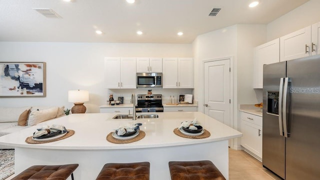 kitchen with stainless steel appliances, a kitchen breakfast bar, a kitchen island with sink, and white cabinets