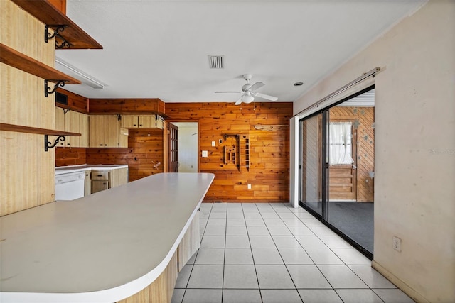 kitchen featuring light tile patterned flooring, wooden walls, dishwasher, ceiling fan, and kitchen peninsula