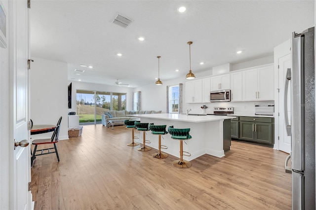 kitchen featuring pendant lighting, light hardwood / wood-style flooring, a breakfast bar, appliances with stainless steel finishes, and a kitchen island with sink