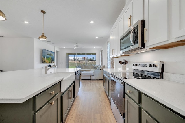 kitchen with sink, appliances with stainless steel finishes, hanging light fixtures, white cabinets, and light wood-type flooring