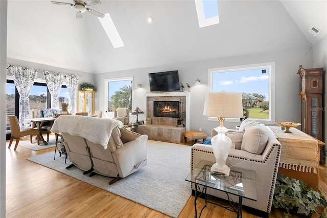 living room featuring hardwood / wood-style flooring, high vaulted ceiling, a high end fireplace, and a skylight