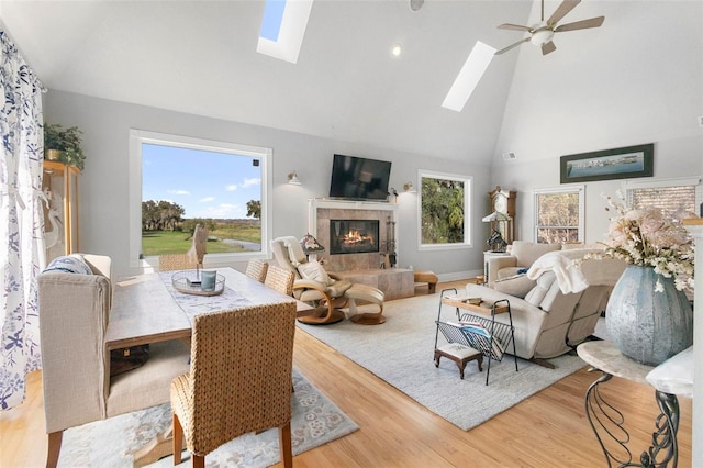 living room with light hardwood / wood-style flooring, ceiling fan, a skylight, high vaulted ceiling, and a fireplace