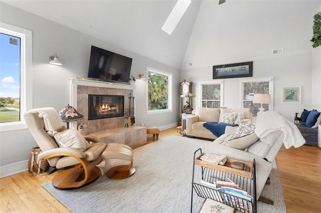 living room featuring high vaulted ceiling, a skylight, a tile fireplace, and wood-type flooring