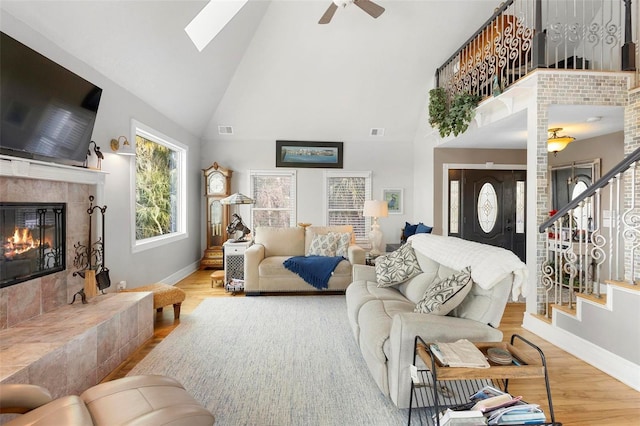 living room with a skylight, a fireplace, high vaulted ceiling, and light wood-type flooring