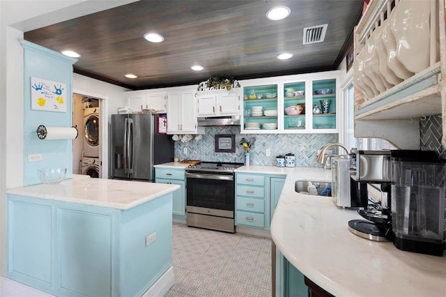 kitchen with appliances with stainless steel finishes, white cabinetry, sink, stacked washer / drying machine, and kitchen peninsula