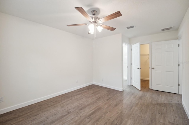 unfurnished bedroom with hardwood / wood-style floors, ceiling fan, a closet, and a walk in closet