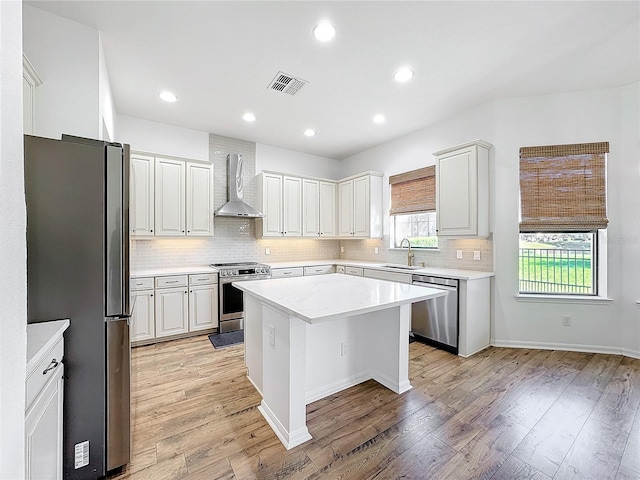 kitchen featuring a kitchen island, white cabinets, light hardwood / wood-style floors, stainless steel appliances, and wall chimney exhaust hood