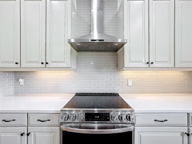 kitchen with white cabinetry, stainless steel electric stove, decorative backsplash, and wall chimney range hood