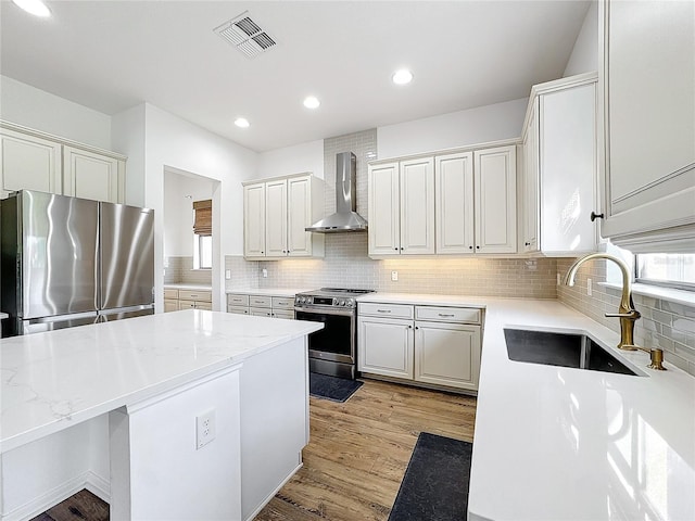 kitchen featuring sink, appliances with stainless steel finishes, white cabinetry, light stone counters, and wall chimney exhaust hood