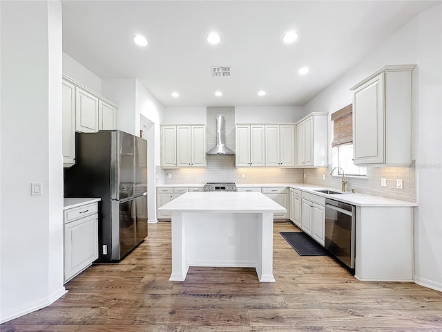 kitchen featuring sink, stainless steel appliances, white cabinets, a kitchen island, and wall chimney exhaust hood