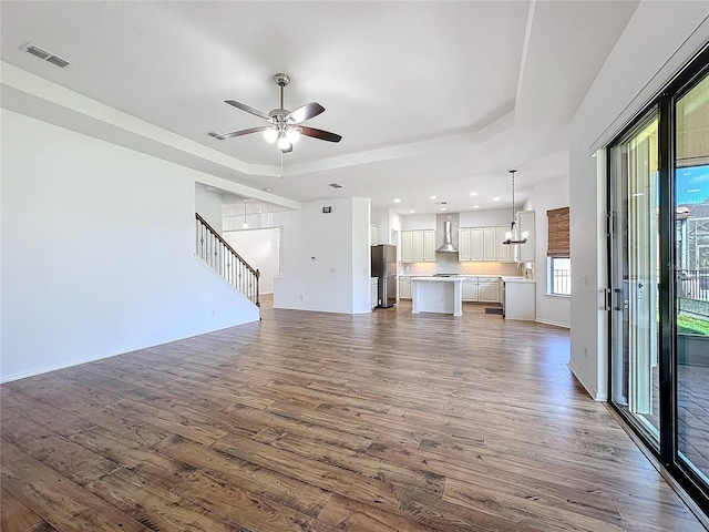 unfurnished living room with dark wood-type flooring, ceiling fan, and a tray ceiling