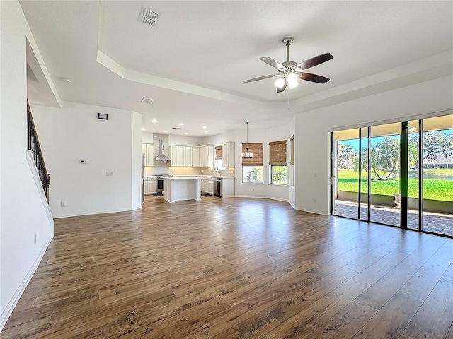 unfurnished living room with dark wood-type flooring, ceiling fan, and a tray ceiling