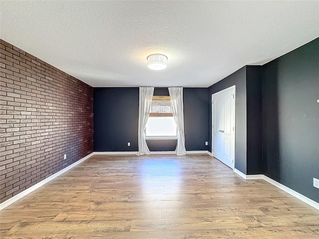 unfurnished room with brick wall, a textured ceiling, and light hardwood / wood-style floors