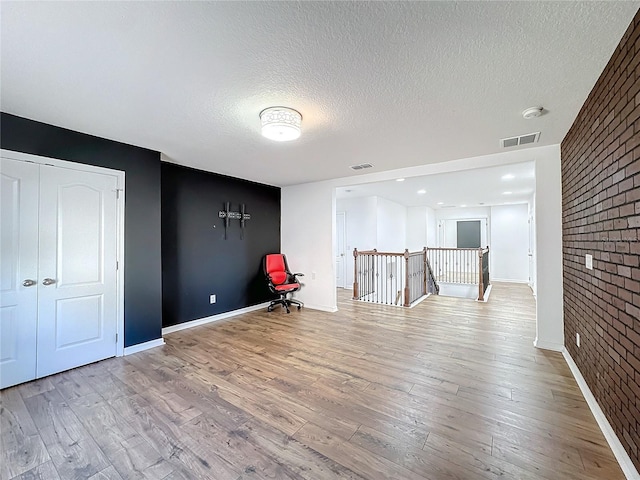 spare room with light hardwood / wood-style flooring, a textured ceiling, and brick wall