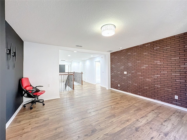 empty room featuring brick wall, a textured ceiling, and light wood-type flooring