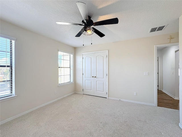 unfurnished bedroom with ceiling fan, light colored carpet, a textured ceiling, and a closet