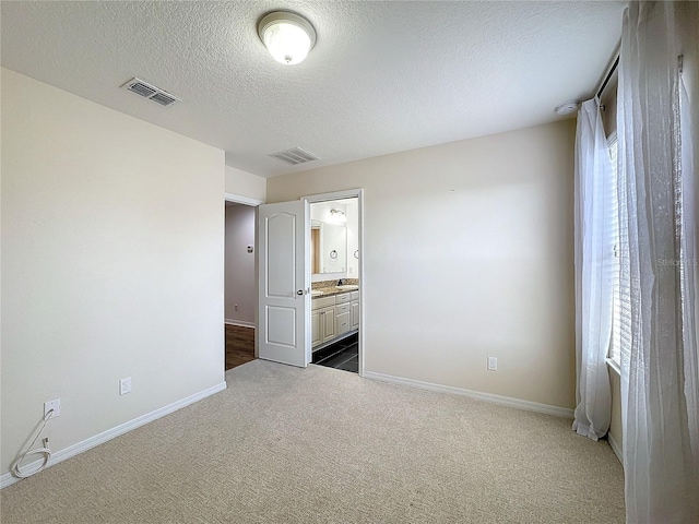 unfurnished bedroom with ensuite bath, carpet, and a textured ceiling