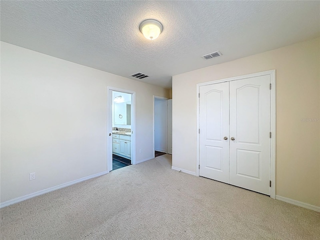 unfurnished bedroom with a closet, connected bathroom, carpet, and a textured ceiling