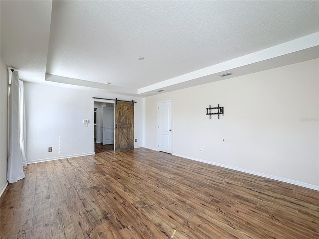 spare room with a raised ceiling, hardwood / wood-style floors, a barn door, and a textured ceiling