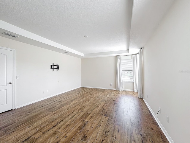 empty room featuring a raised ceiling, hardwood / wood-style floors, and a textured ceiling