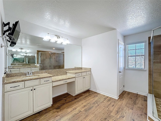 bathroom featuring wood-type flooring, a shower with door, vanity, and a textured ceiling