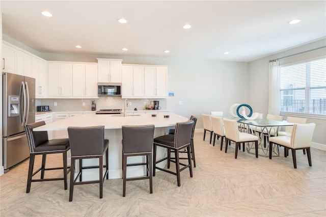 kitchen featuring tasteful backsplash, stainless steel fridge with ice dispenser, white cabinets, and a center island with sink