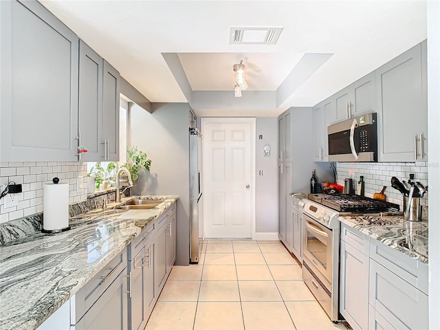 kitchen featuring light tile patterned flooring, sink, light stone counters, appliances with stainless steel finishes, and a tray ceiling