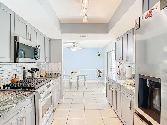 kitchen featuring gray cabinetry, light tile patterned floors, a raised ceiling, stainless steel appliances, and decorative backsplash