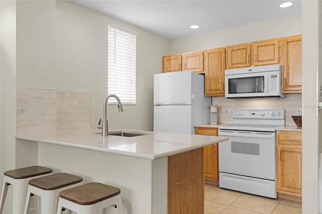 kitchen featuring light tile patterned flooring, sink, a kitchen breakfast bar, kitchen peninsula, and white appliances