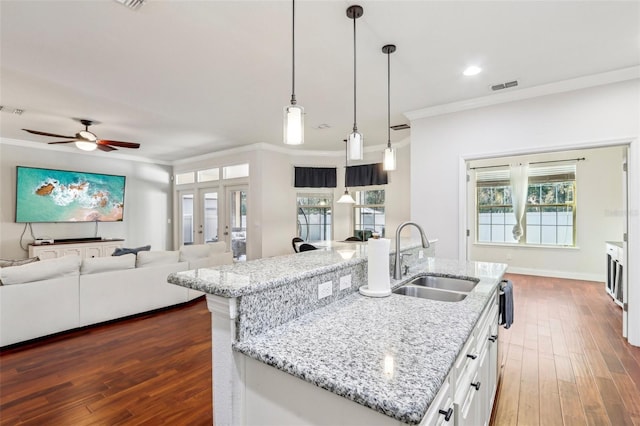 kitchen with pendant lighting, sink, white cabinets, a kitchen island with sink, and light stone countertops