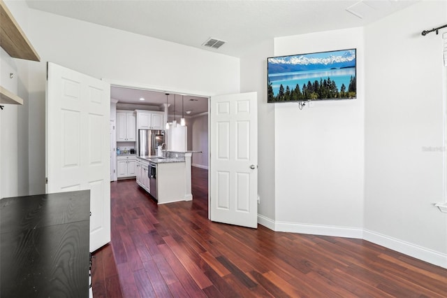 interior space with dark wood-type flooring, white cabinetry, light stone counters, decorative light fixtures, and a kitchen island