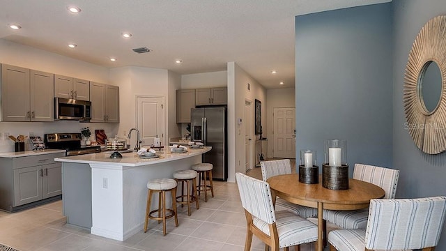 kitchen with light tile patterned flooring, sink, gray cabinetry, a center island with sink, and stainless steel appliances