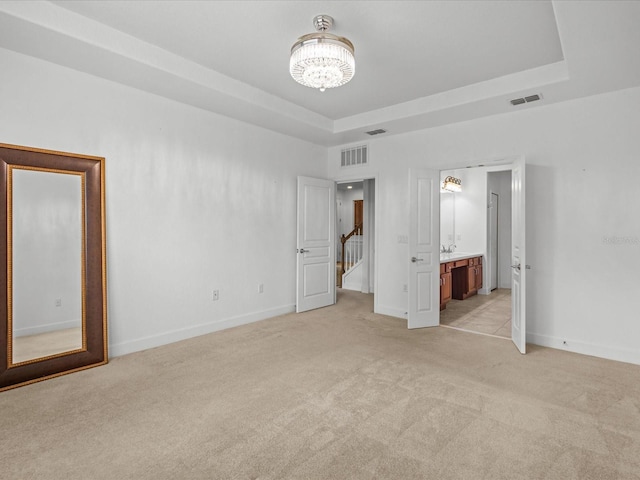 1431 Milledge Ln, Davenport, FL 33896 - unfurnished bedroom with ensuite bathroom, light colored carpet, an inviting chandelier, and a tray ceiling