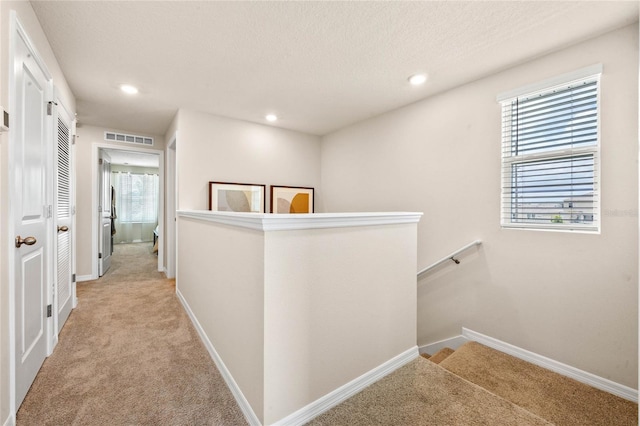 hall featuring light carpet and a textured ceiling