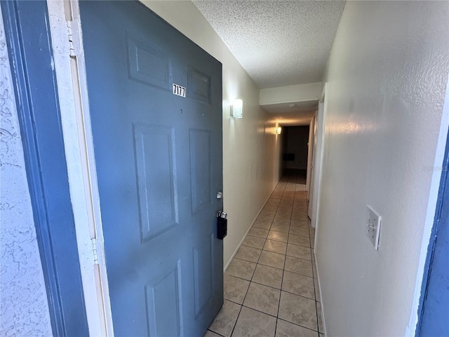 hallway with a textured ceiling and light tile patterned flooring