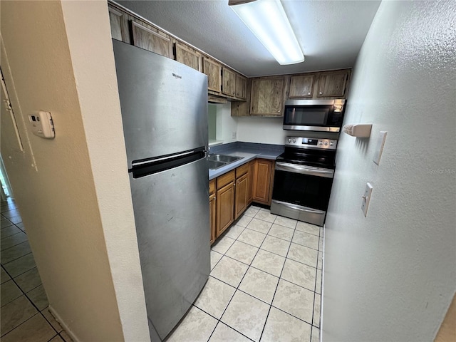 kitchen with appliances with stainless steel finishes, sink, light tile patterned floors, and a textured ceiling