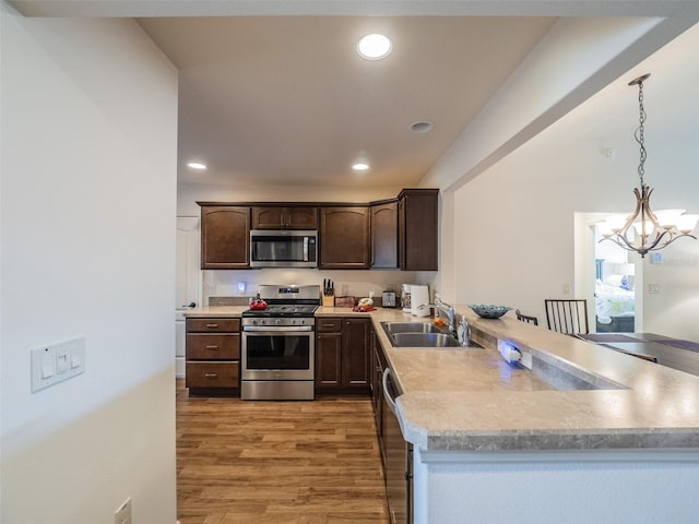 kitchen with sink, decorative light fixtures, light hardwood / wood-style flooring, kitchen peninsula, and stainless steel appliances