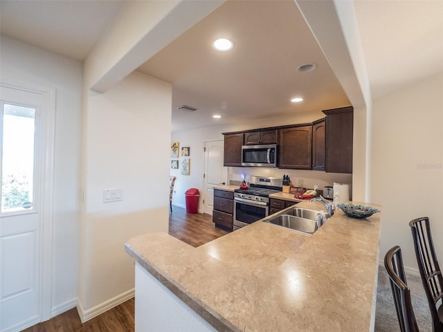 kitchen featuring sink, stainless steel appliances, dark hardwood / wood-style floors, dark brown cabinetry, and kitchen peninsula