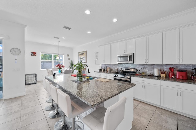 kitchen with appliances with stainless steel finishes, a breakfast bar, a kitchen island with sink, and dark stone counters