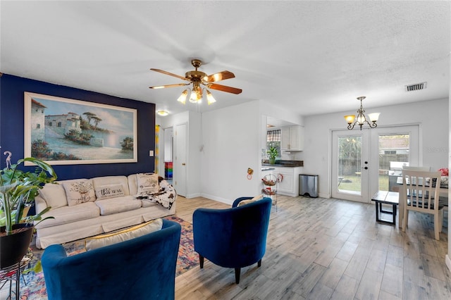 living room featuring french doors, ceiling fan with notable chandelier, a textured ceiling, and light hardwood / wood-style flooring