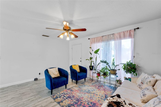 living area with ceiling fan, a textured ceiling, and light wood-type flooring