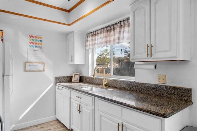 kitchen featuring sink, dark stone countertops, white cabinets, white refrigerator, and light hardwood / wood-style floors