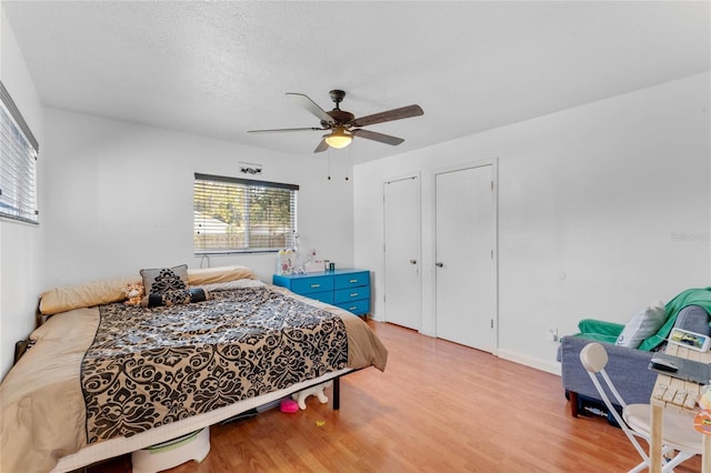 bedroom featuring ceiling fan, a textured ceiling, light hardwood / wood-style floors, and multiple closets