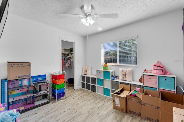 rec room with ceiling fan, a textured ceiling, and light hardwood / wood-style flooring